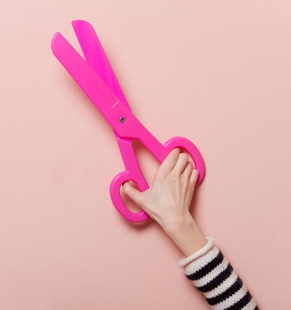Hand holding pink scissors on pink backgroundの写真素材