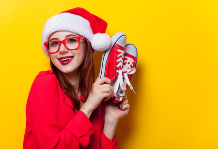 Portrait of a young redhead woman in Santa Claus hat and with gumshoes on yellow backgroundの写真素材