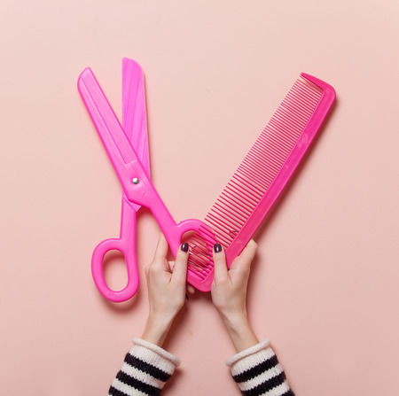 Hand holding pink scissors and comb on pink backgroundの写真素材