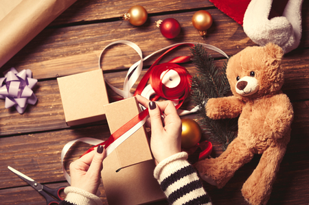 Female hands are wrapping a christmas gift on wooden backgroundの写真素材
