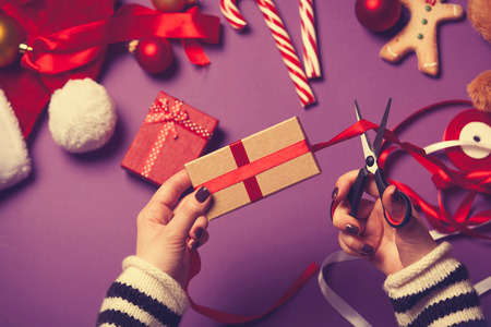 Female hands are wrapping a christmas gift on violet backgroundの写真素材