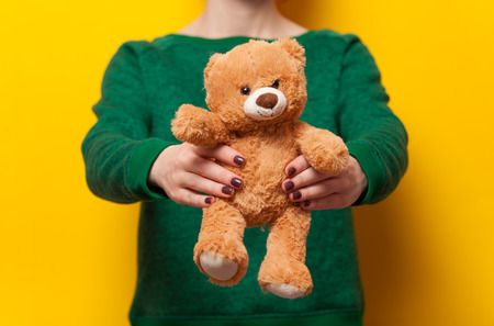 Woman holding teddy bear toy on yellow backgroundの写真素材