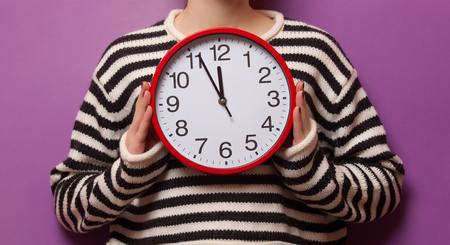 Woman holding alarm clock on violet backgroundの写真素材