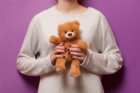 Woman holding teddy bear toy on violet backgroundの写真素材