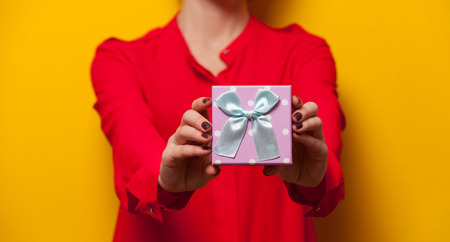 Woman holding a present box on yellow backgroundの写真素材