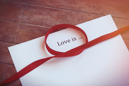 Paper with words Love is and ribbon on wooden backgroundの写真素材