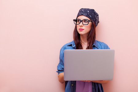 portrait of beautiful young woman in glasses with laptop standing on the pink backgroandの写真素材