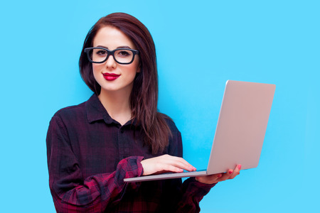 portrait of beautiful young woman in glasses with laptop standing on the blue backgroundの写真素材