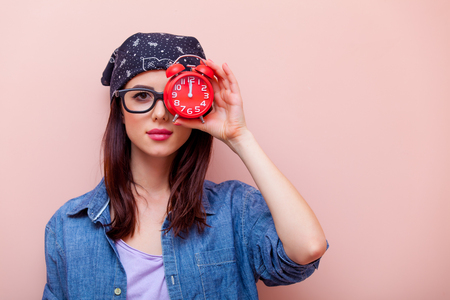 portrait of beautiful young woman with a red alarm clock standing on the pink backgroundの写真素材