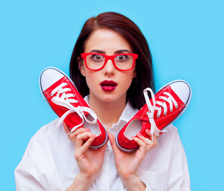 portrait of beautiful young woman with red gumshoes standing on the blue backgroundの写真素材