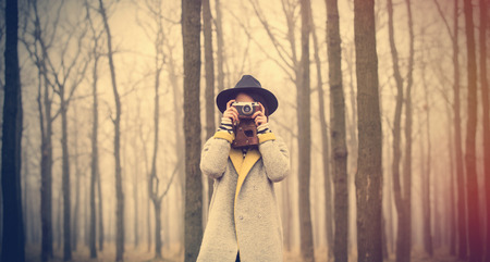 portrait of a young woman with a camera standing in the middle of the forestの写真素材