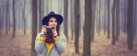 portrait of a young woman with a camera standing in the middle of the forest