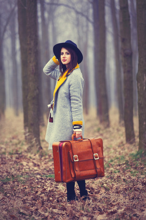 portrait of a young woman with a camera and suitcase standing in the middle of the forestの写真素材