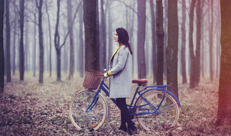 portrait of a young woman with a bicycle and suitcase standing in the middle of the forestの写真素材