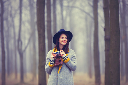 portrait of a young woman with a camera standing in the middle of the forestの写真素材