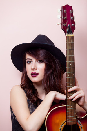 portrait of a beautiful young woman with brown guitar standing on the pink backgroundの写真素材