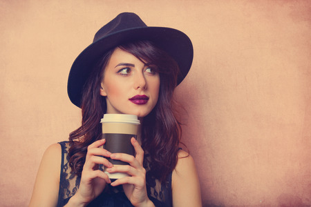 portrait of a beautiful young woman with a cup of coffee standing on the pink backgroundの写真素材