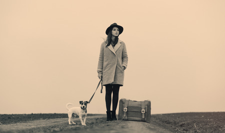 portrait of a young beautiful woman with suitcase and dog standing in the field