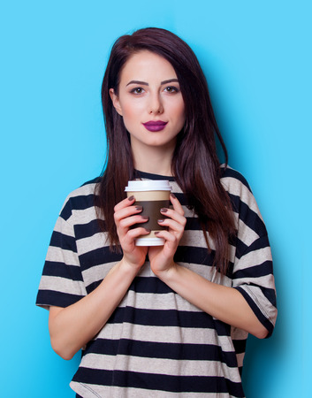 portrait of a young beautiful woman with cup of coffee standing on the blue backgroundの写真素材