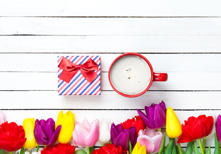 colorful tulips, red cup and gift on the white wooden tableの写真素材