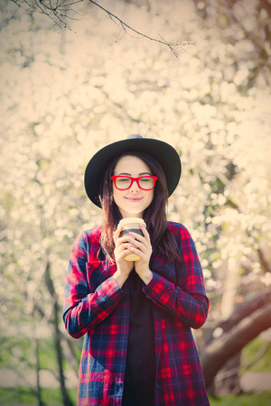 portrait of the beautiful young woman with cup of coffee near blooming cherryの写真素材
