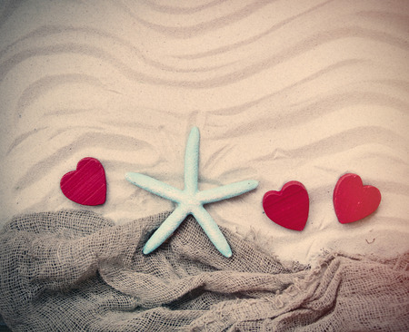 blue starfish, red wooden hearts and fishnet lying on the sandの写真素材