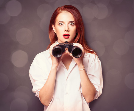 Portrait of a surprised businesswomen in white shirt with binocular on grey background.の写真素材
