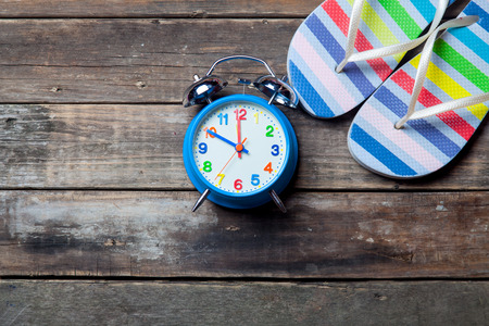 photo of the blue clock and colorful sandals on the brown wooden backgroundの写真素材