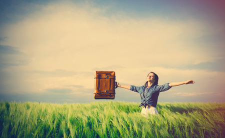 portrait of young beautiful woman with suitcase in the fieldの写真素材