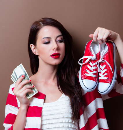 portrait of beautiful young woman with red gumshoes and money on the brown backgroundの写真素材