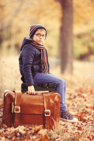 portrait of the little boy with a big suitcase sitting on the bench in the parkの写真素材