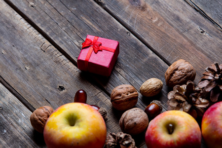 photo of the delicious apples, red gift, fir-cones and nuts on the brown wooden backgroundの写真素材
