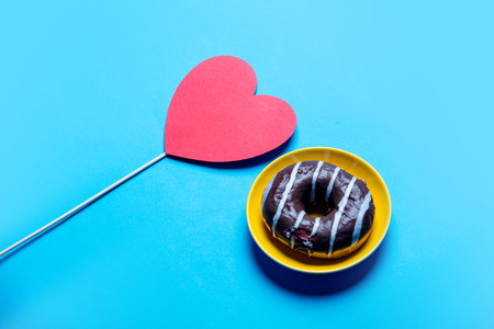photo of the chocolate donut on the plate and red heart shaped toy on the blue backgroundの写真素材