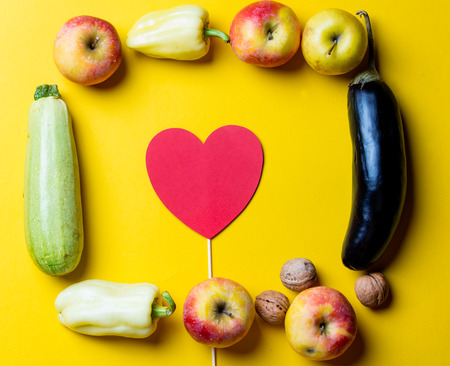 photo of the fresh vegetables, nuts, fruits and heart shaped toy on the yellow backgroundの写真素材