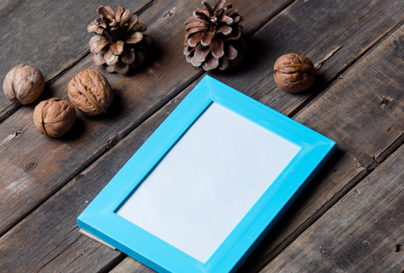 photo of the blue photo frame, nuts and fir-cones on the brown wooden background