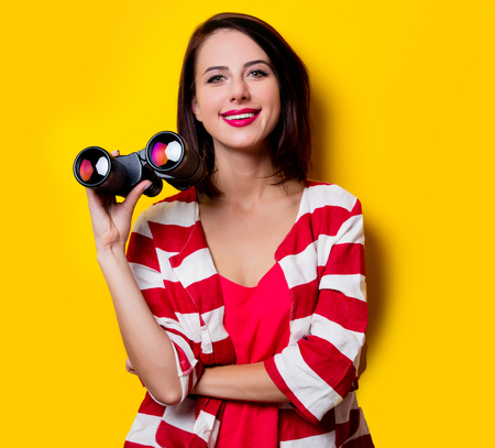 portrait of the beautiful young woman with binoculars on the yellow backgroundの写真素材