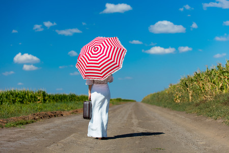 photo of the beautiful young woman with suitcase and umbrella walking on the roadの写真素材