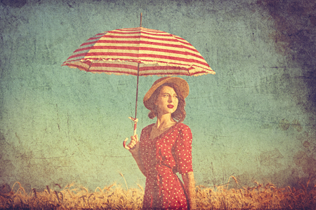 portrait of the beautiful young woman with red umbrella standing in the fieldの写真素材