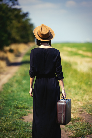 photo of the beautiful young woman with suitcase on the countryside roadの写真素材