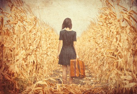 photo of the beautiful young woman with suitcase standing in the middle of the fieldの写真素材