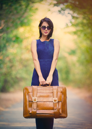 portrait of the beautiful young woman with suitcase standing in the middle of the roadの写真素材
