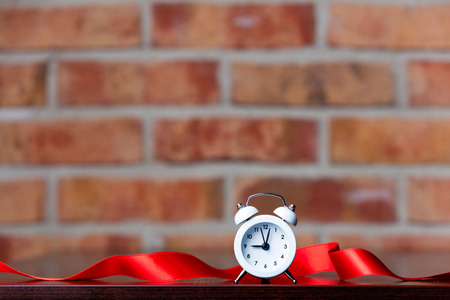Ribbon and little alarm clock on brick wall backgroundの写真素材