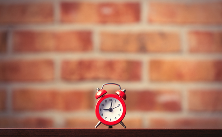 little red alarm clock on table with brick wall on backgroundの写真素材
