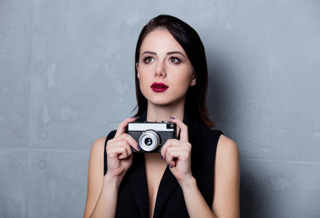 Portrait of a style brunette woman with vintage photo camera on grey backgroundの写真素材