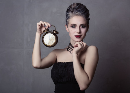 Portrait of young woman in witch halloween costume with alarm clock, smiling over grey backgroundの写真素材