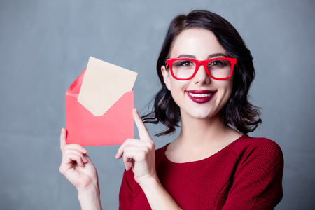 Portrait of young woman in black dress with envelope Christmas gift over grey background