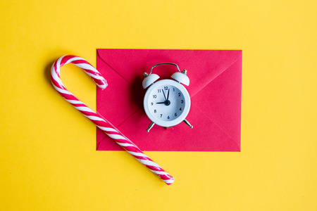 Christmas alarm clock and lolipop with red envelope on yellow backgroundの写真素材