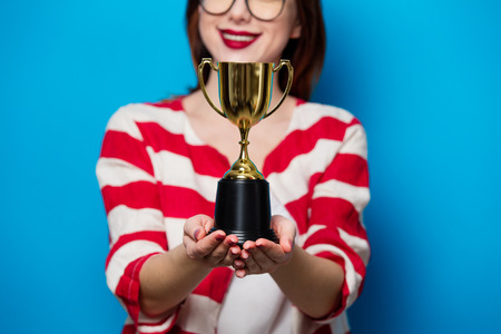portrait of the beautiful young smiling woman with cup trophy on the blue backgroundの写真素材