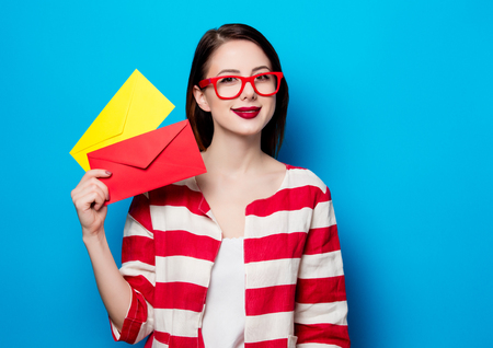 portrait of beautiful young smiling woman with two envelopes on blue backgroundの写真素材