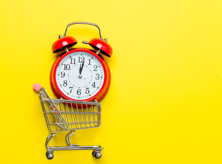 red alarm clock in the small shopping cart on the beautiful yellow backgroundの写真素材
